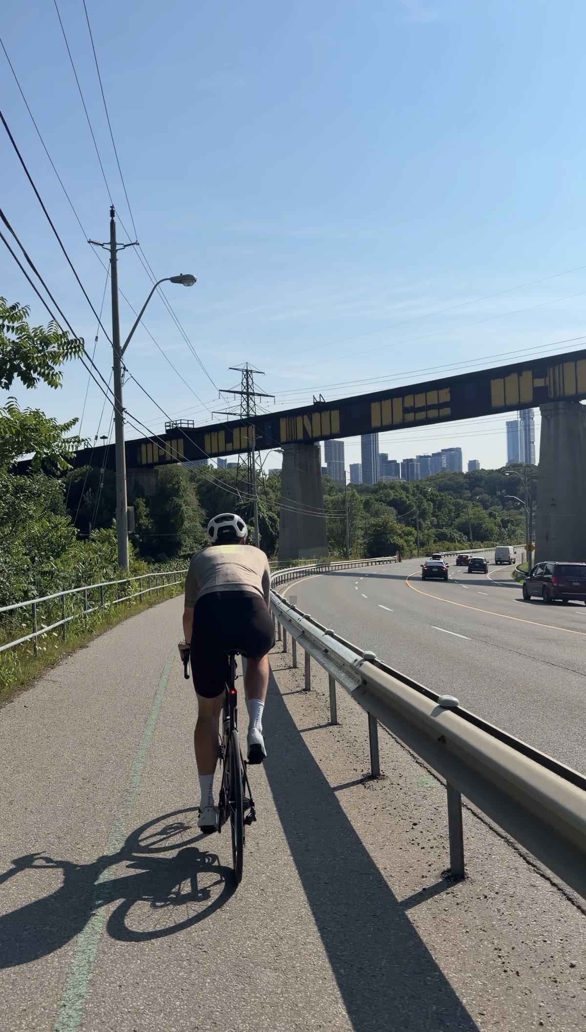 A rider on the paved path beside the Don Valley Parkway, rail bridge and skyline behind