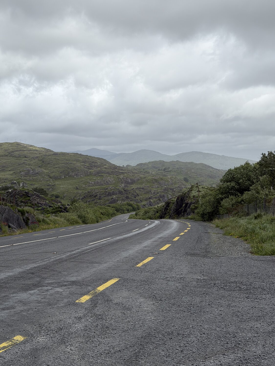 A sweeping empty road on the Beara curving toward distant mountains under a grey sky