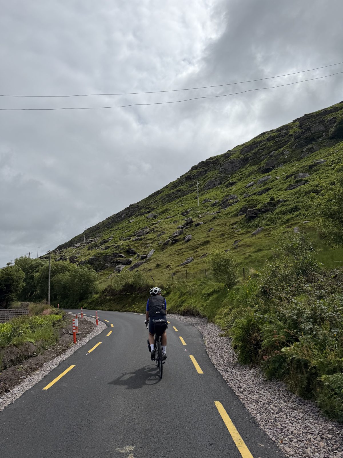 A rider climbing a quiet road below a green and rocky Kerry hillside