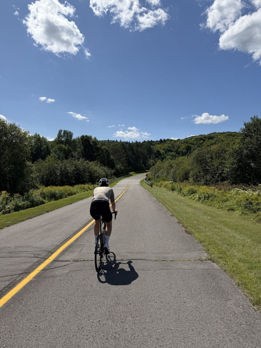A rider on an open rolling stretch of parkway in Gatineau Park under a blue sky