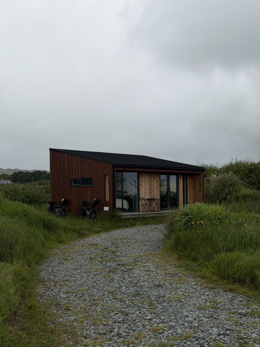 The timber eco cabin at Goleen Harbour with the two loaded bikes parked at the door, up a gravel path through long grass