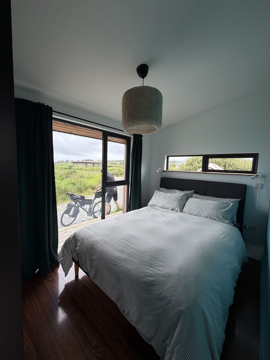 The cabin bedroom with a big window looking out over the fields and a bike parked on the deck