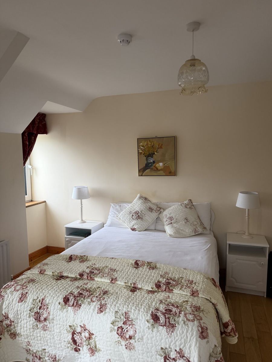 A cosy double bedroom with a floral quilt, bedside lamps and a framed print