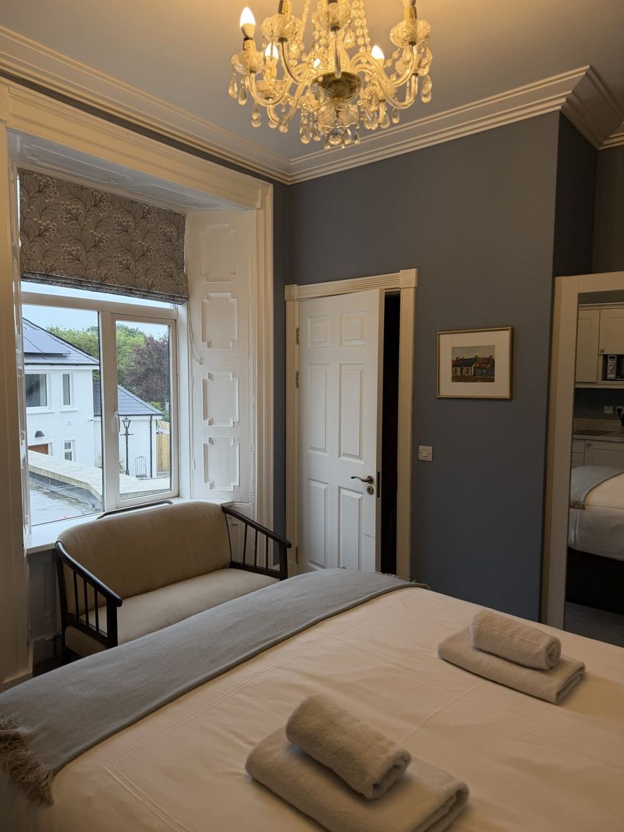 A bedroom at Áras de Staic in Dingle with grey walls, a crystal chandelier and a bright window seat looking onto Green Street