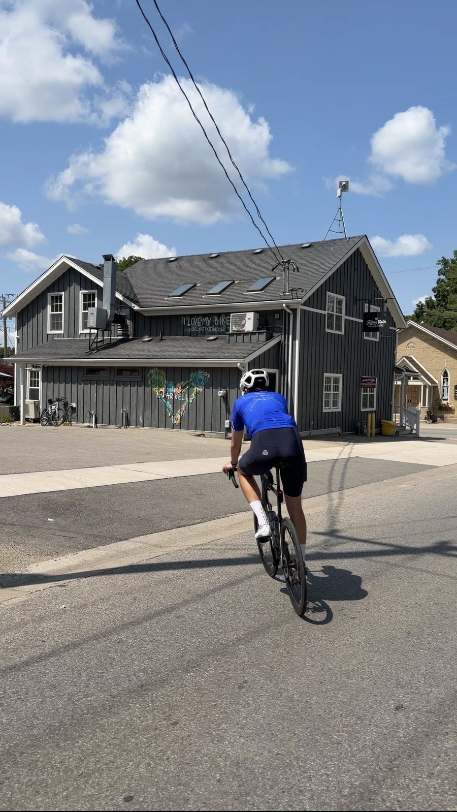Francis riding up to Flow State Bike Co, a dark barn-style building in Arkell with an I love Arkell mural